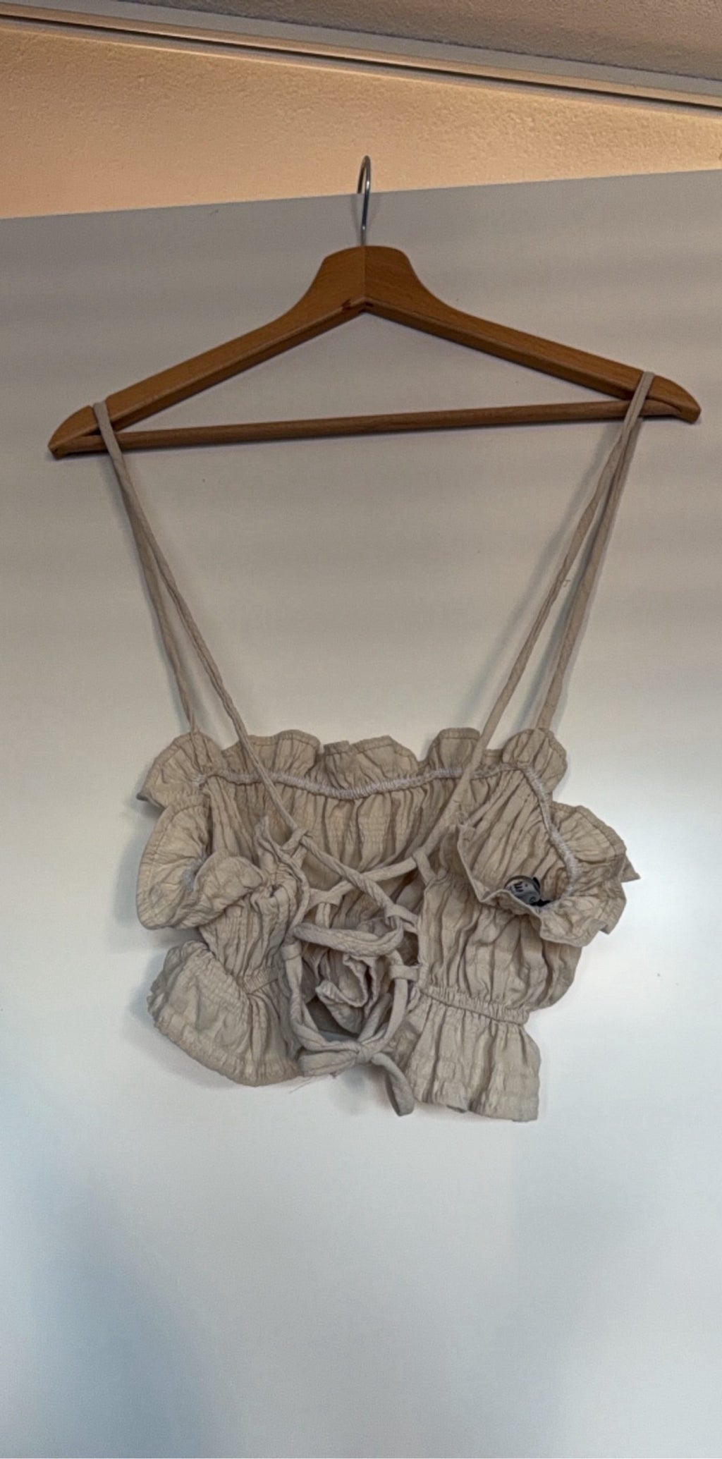 Mai Collection beige crop top with ruffle details and adjustable lace-up back.